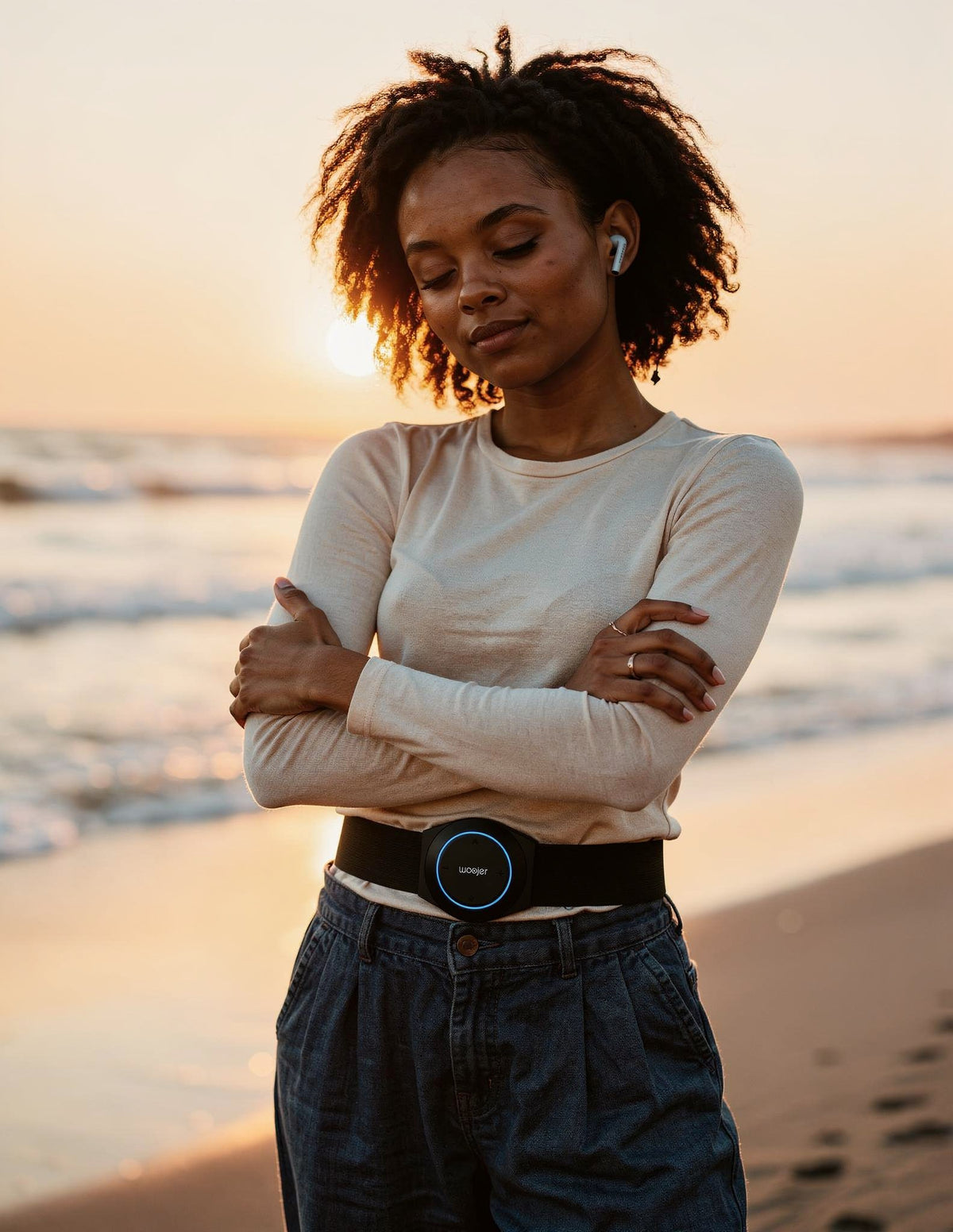 A woman by the ocean with her eyes closed, breathing, wearing the Woojer Strap
